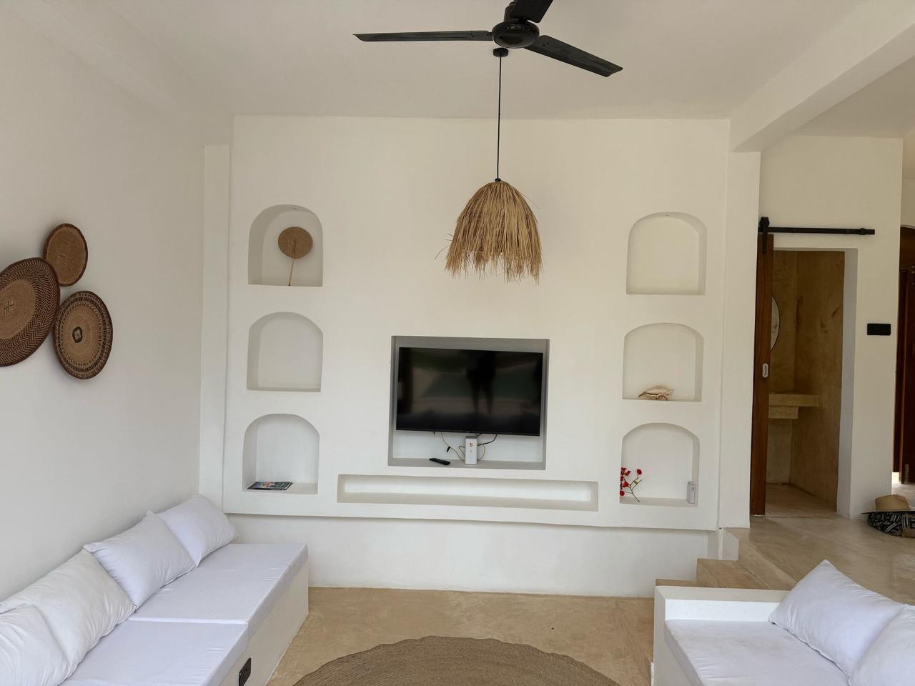 Villa Mawaka coral-stone TV feature wall with arched Swahili niches and pendant lantern